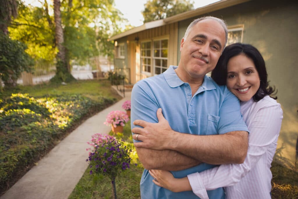 A happy couple in front of an investment property shows that being prepared is the key to successful rental property ownership.
