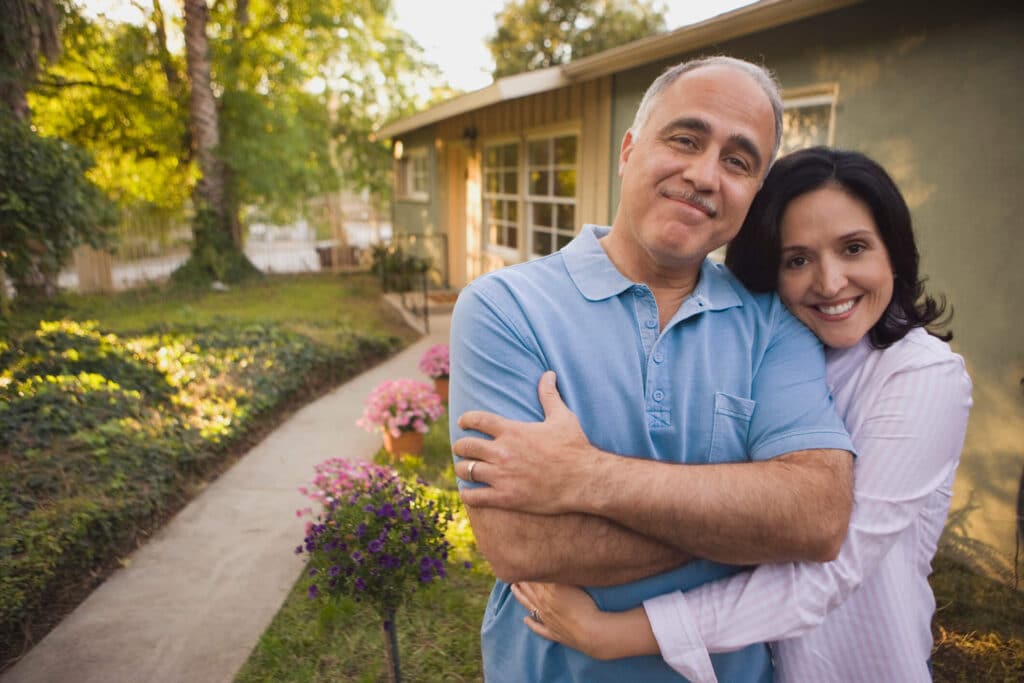 A happy couple in front of an investment property shows that being prepared is the key to successful rental property ownership. 