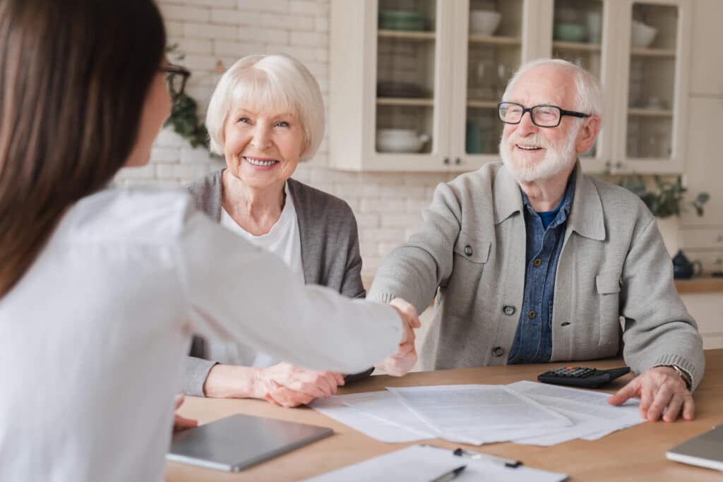 A happy older couple shaking hands with their property manager. 
